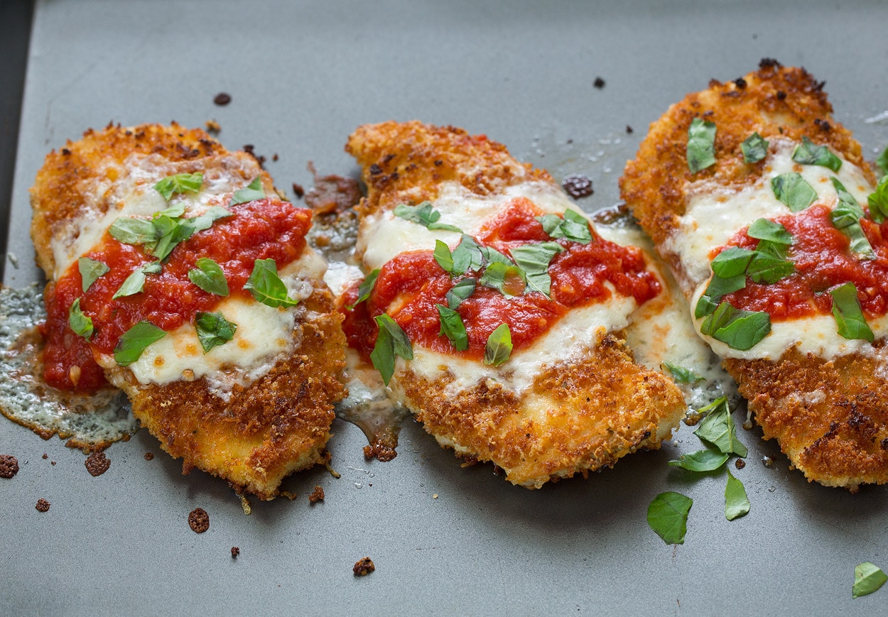 Finished chicken parmesan with cheese marinara and basil after baking. Shown on dark baking sheet.