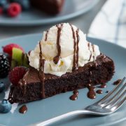 Flourless Chocolate Cake on a blue serving plate. Cake is topped with vanilla ice cream and fudge sauce.