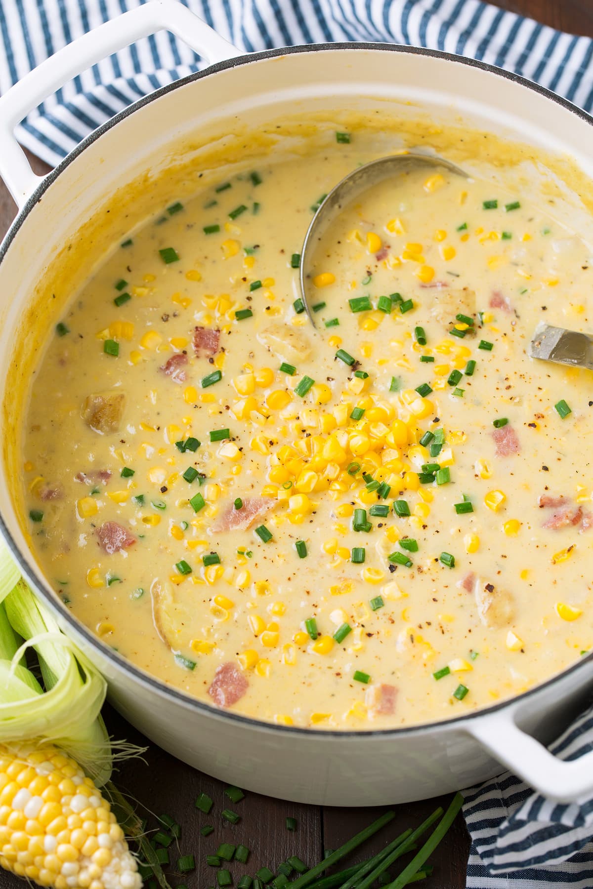 White enamel pot full of corn chowder soup with a ladle in it.