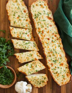 Two halves of cheese garlic bread on a cutting board, one is cut into slices.