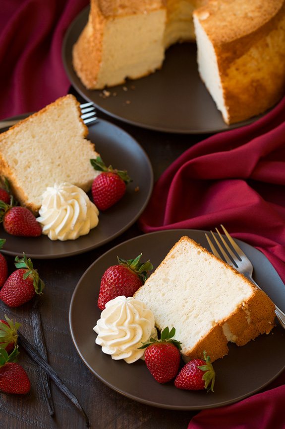 two slices of Vanilla Bean Angel Food Cake on plates with whipped cream and berries
