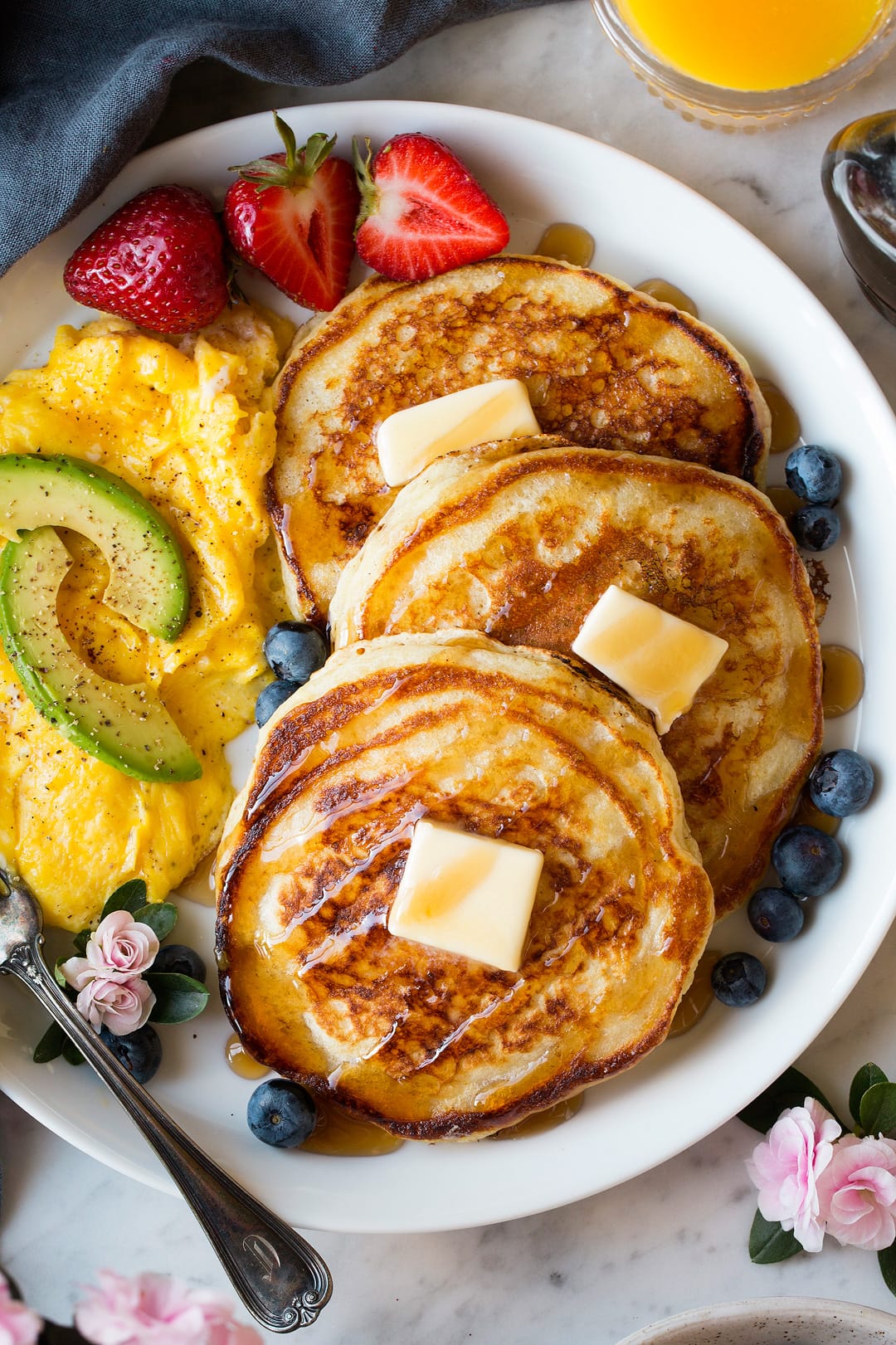 Three buttermilk pancakes on a large white blueberries, strawberries and a side of eggs.