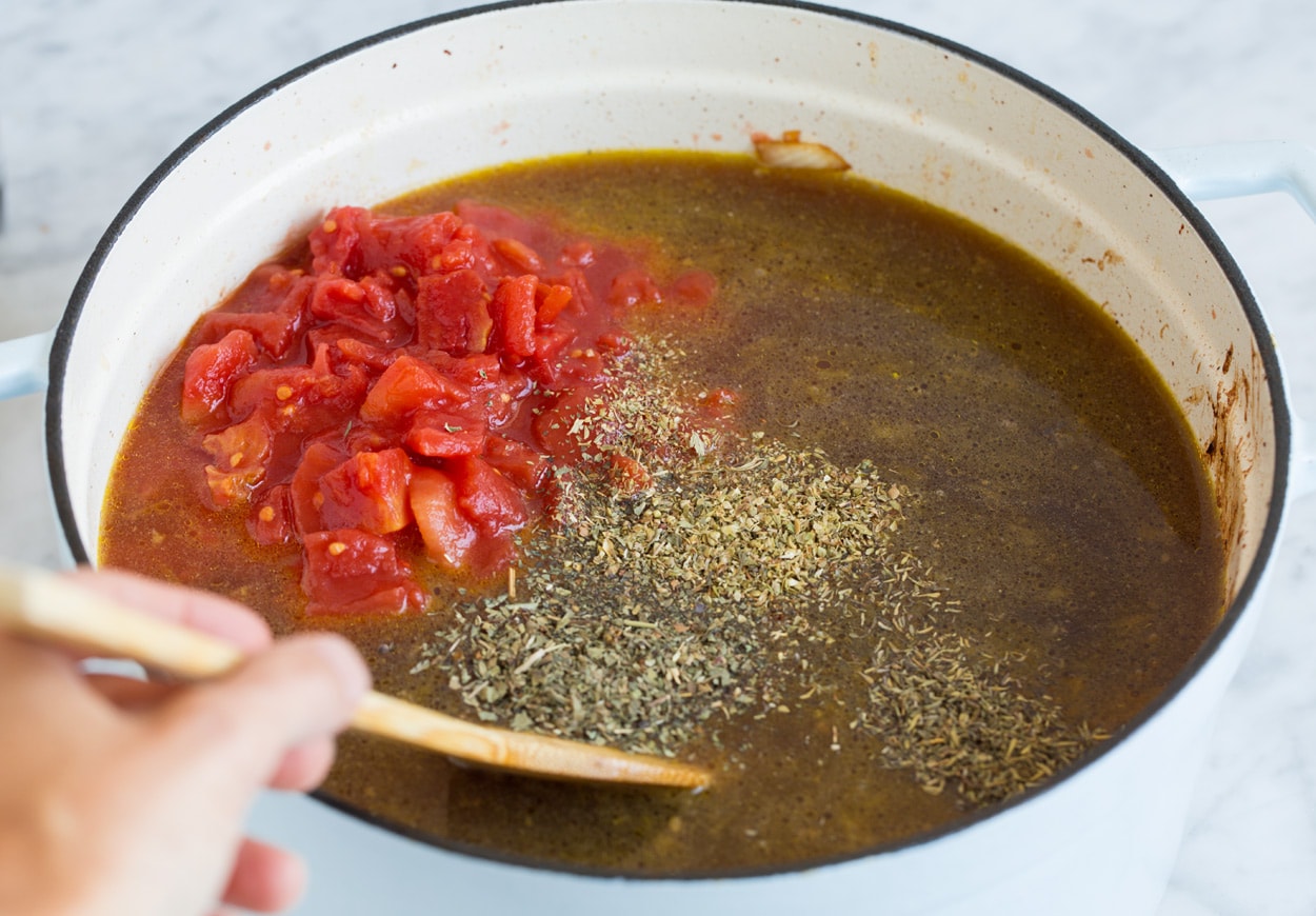 Vegetable Beef Soup adding beef broth tomatoes cooked beef and herbs to mixture in pot