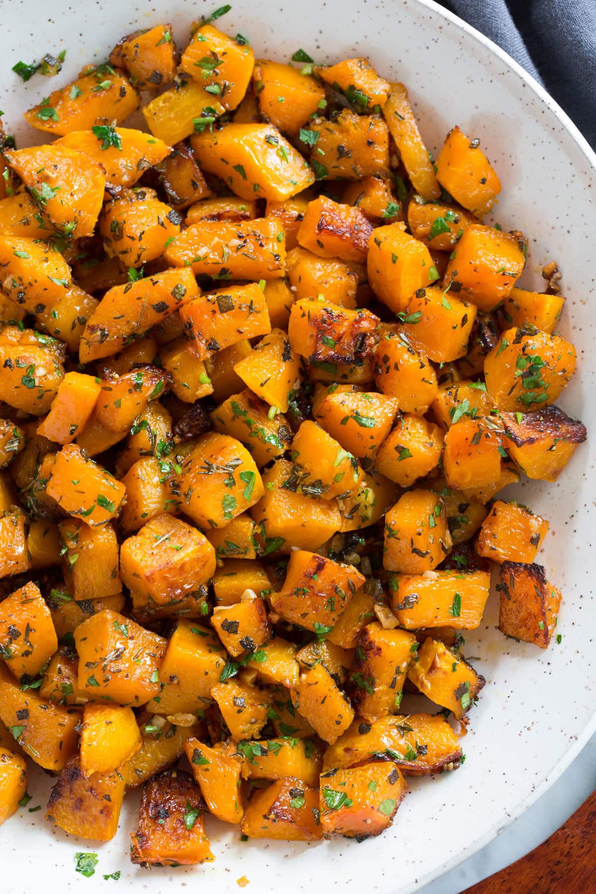 Roasted Butternut Squash in a white ceramic serving bowl set over a white marble surface.