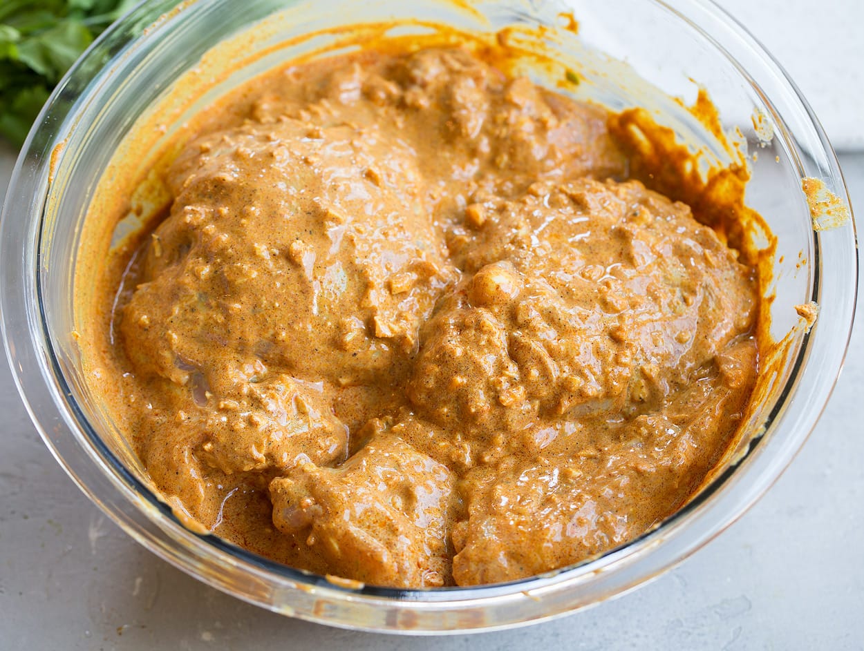Tossing chicken with marinade in glass mixing bowl to make Tandoori Chicken.
