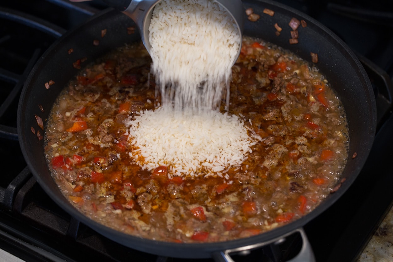 Adding rice to skillet to make Chimichurri Beef and Rice.