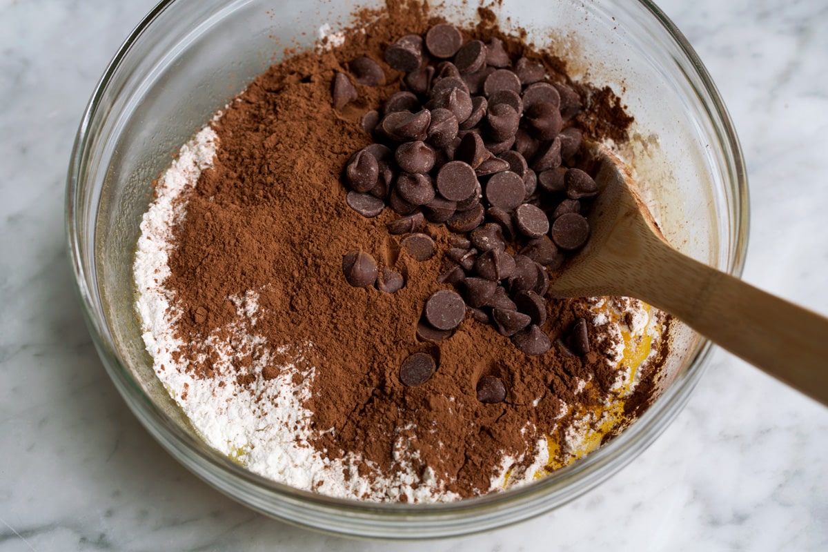Adding flour, cocoa powder and chocolate chips to mixing bowl for brownies.
