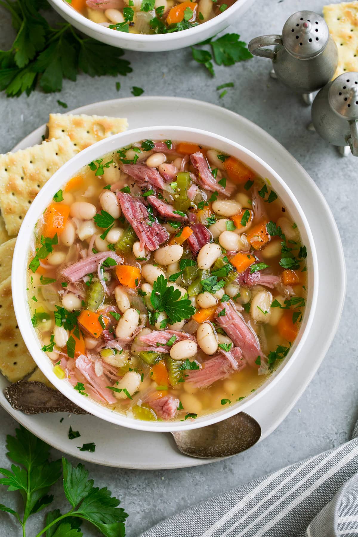 Ham and Bean Soup Overhead image of single serving of ham and bean soup in a white bowl set over a white plate with a side of crackers.