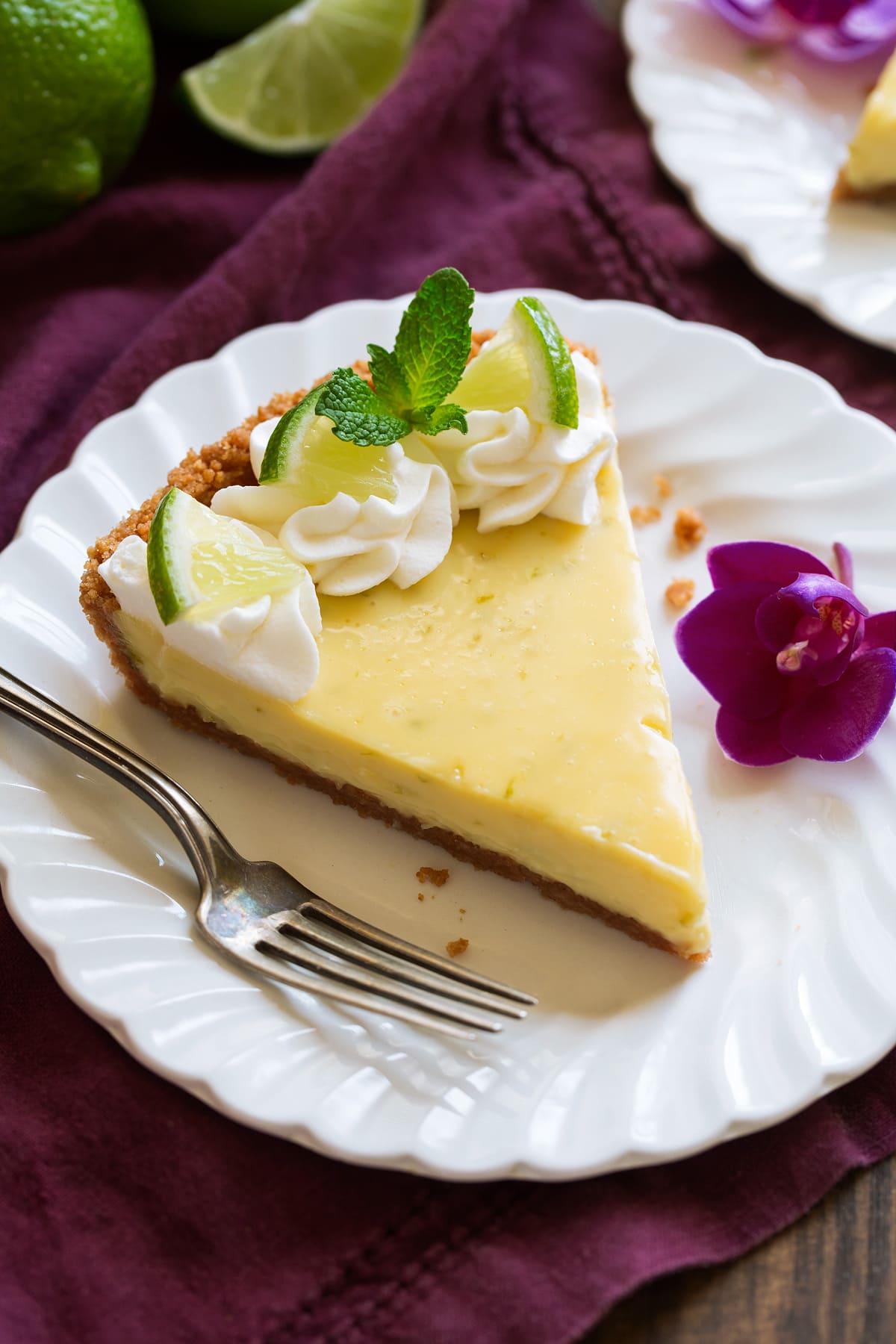 Slice of Best Key Lime Pie on white scalloped dessert plate set over a maroon napkin.