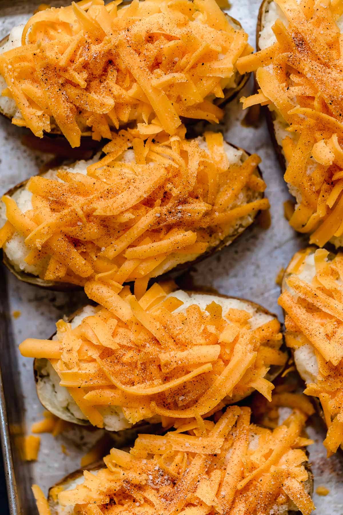 Twice Baked Potatoes Twice baked potatoes filled with mashed potatoes and topped with shredded cheddar and seasoning. Shown before baking.