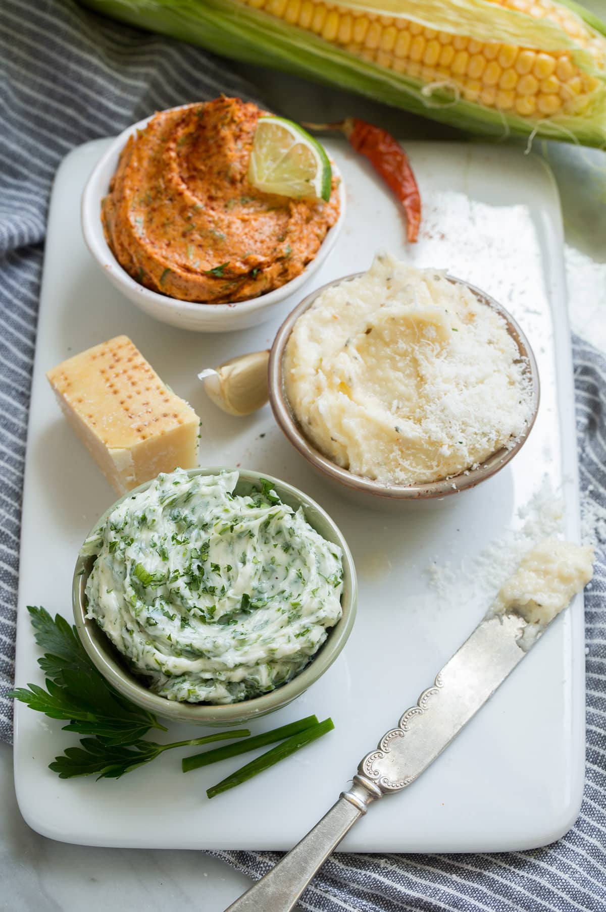 Grilled Corn on the Cob + 3 Flavored Butters Flavored butters in three small ceramic serving bowls set over a white platter.