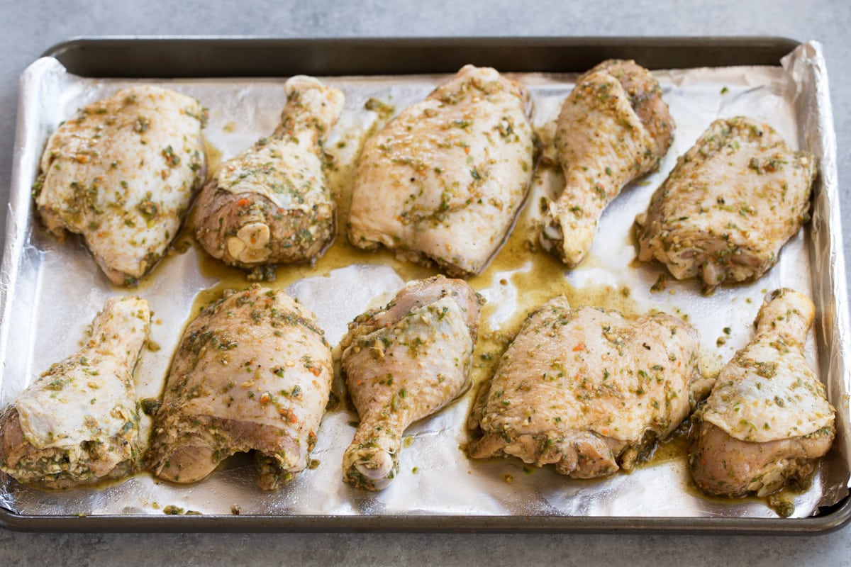 Raw marinated chicken pieces on a foil lined baking sheet.