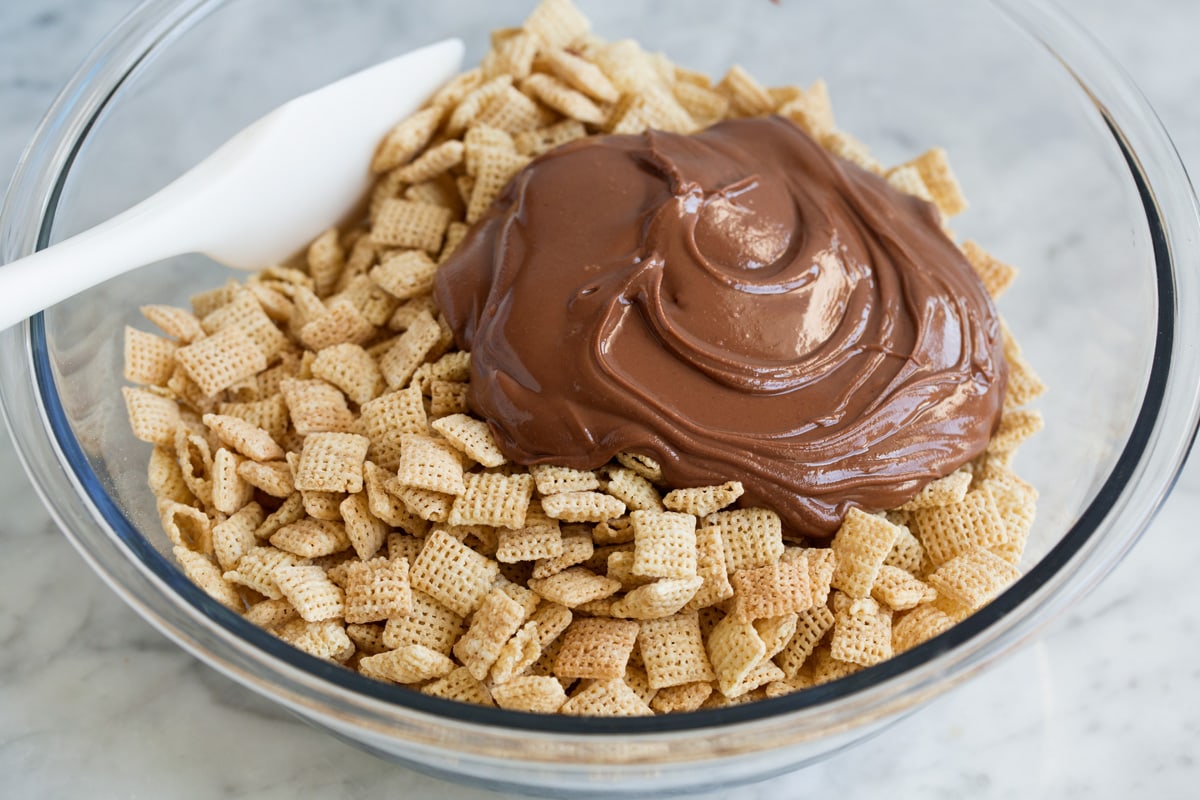 Perfect Puppy Chow {Muddy Buddies}! - one of my go-to treats! These are dangerously addictive! Perfect for parties, holidays and traveling too. #muddybuddies #puppychow #treat #chocolate #chex #peanutbutter Adding chocolate mixture to chex cereal in a mixing bowl.