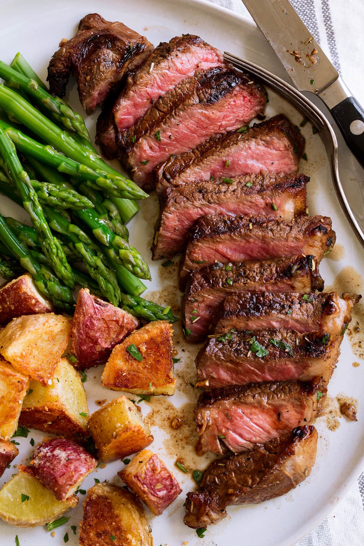 Marinated grilled steak on a serving plate with a side of asparagus and potatoes.