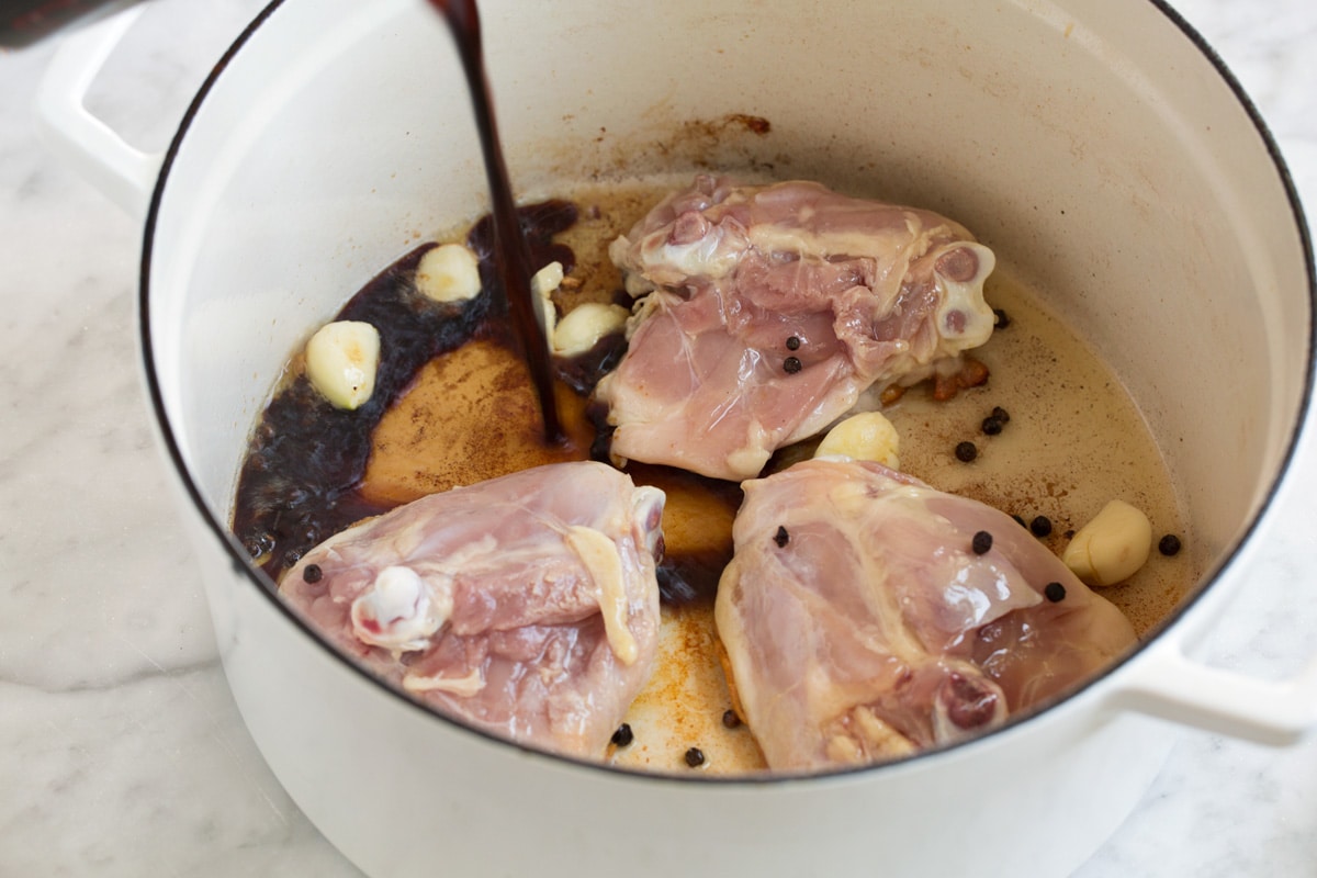Chicken Adobo - easy Filipino chicken recipe made with soy sauce, vinegar, garlic and a hint of brown sugar. Tastes similar to teriyaki sauce but not quite so sweet. A perfect weeknight dinner! #chicken #adobo #recipe Pouring soy sauce and vinegar mixture into pot with chicken thighs, garlic and peppercorn.