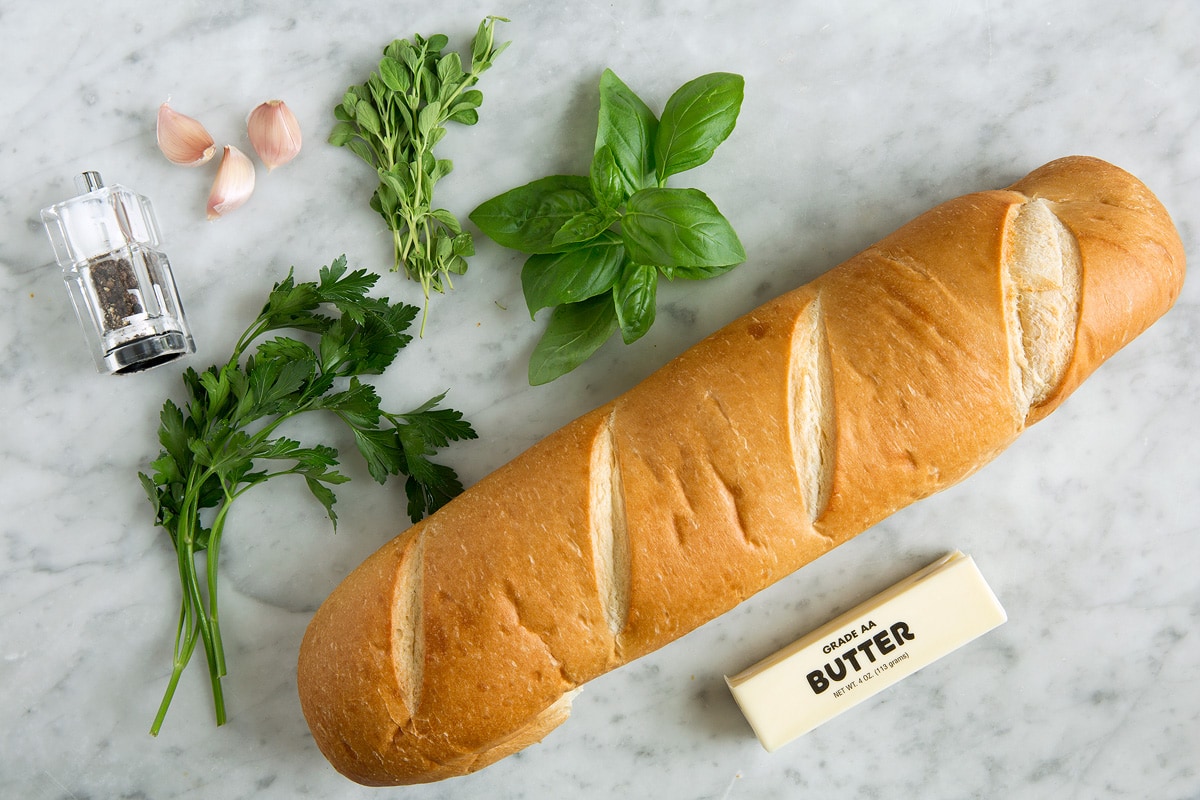Garlic Bread - super fast, super easy and incredibly flavorful! Skip the margarine coated garlic bread from the store and make this butter version instead, it's a hundred times better! #garlicbread #sidedish #bread #appetizer Ingredients for garlic bread including french bread loaf, garlic, butter, and fresh herbs.