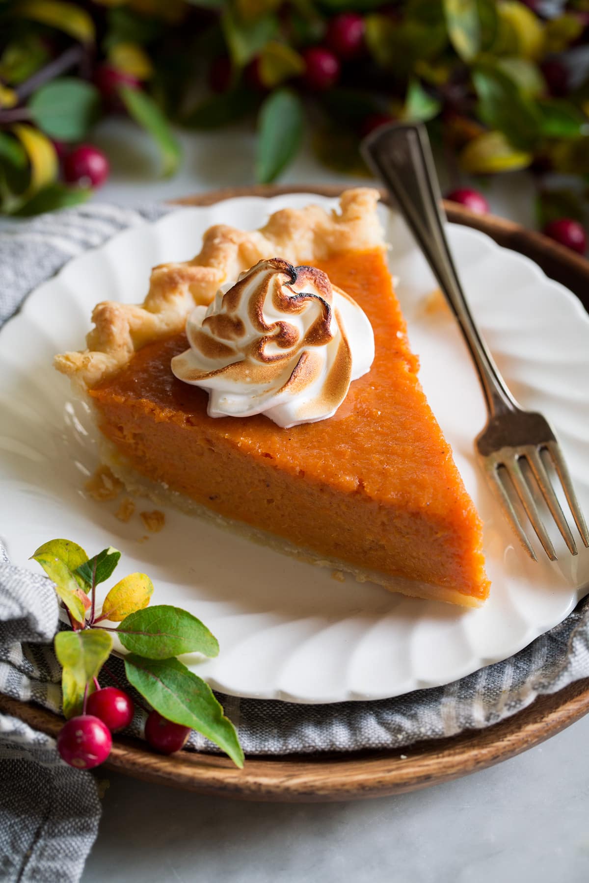 Slice of sweet potato pie on a white dessert plate. Pie is topped with toasted marshmallow topping.