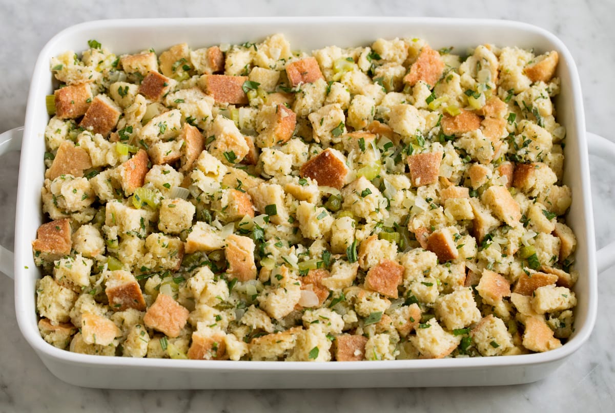 Raw stuffing mixture spread in white baking dish shown before baking.