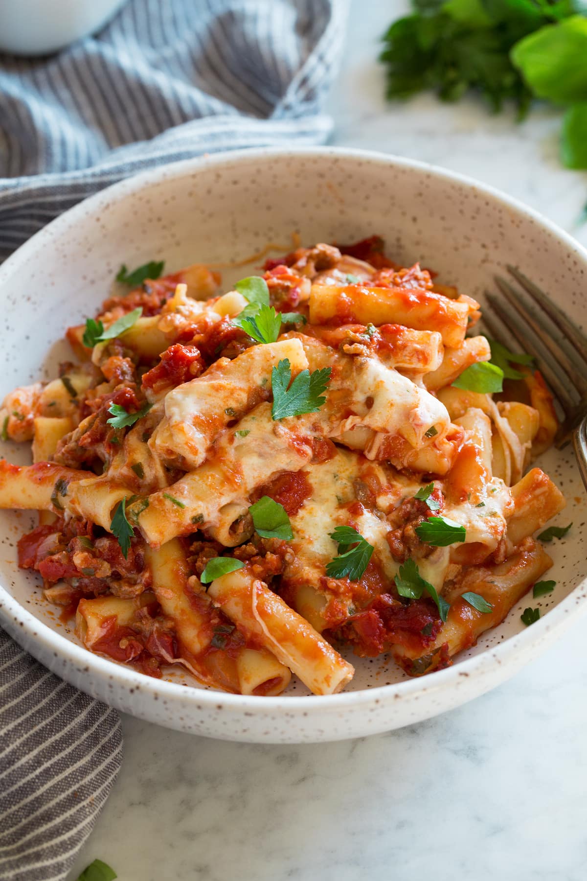 Single serving of baked ziti in a pasta bowl, garnished with fresh parsley on top.