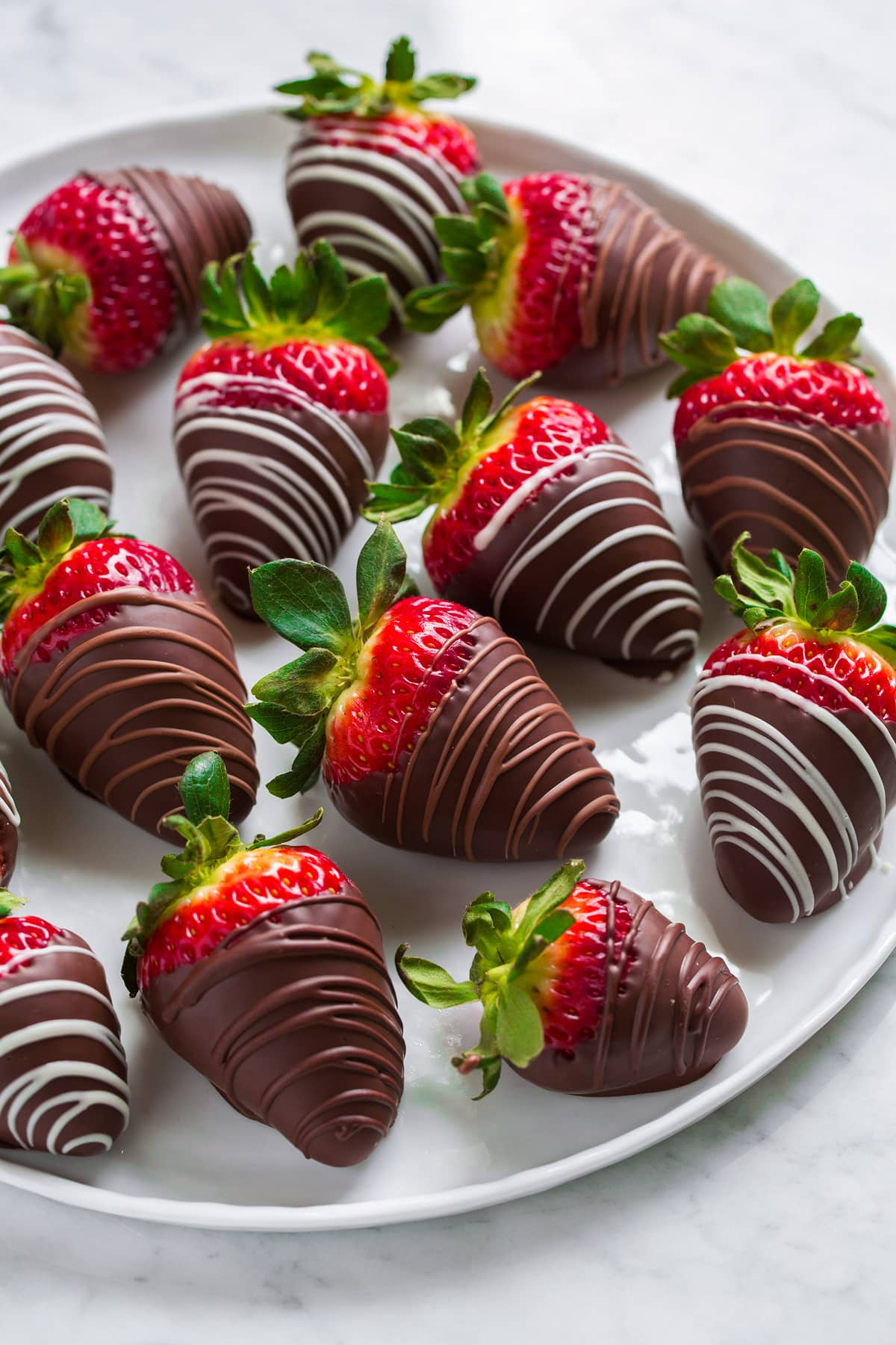 Side view of chocolate covered strawberries sitting on a white serving platter on a marble surface.
