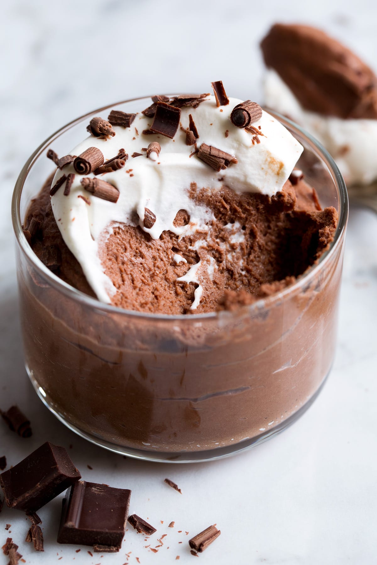 Close up image of chocolate mousse covered with whipped cream. Spoonful removed to show fluffy texture of interior.