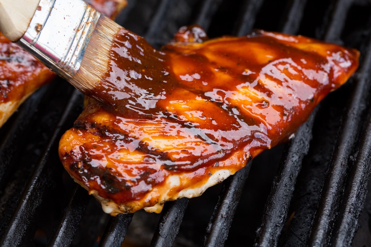Homemade BBQ Sauce Basting chicken breast on grill with bbq sauce.