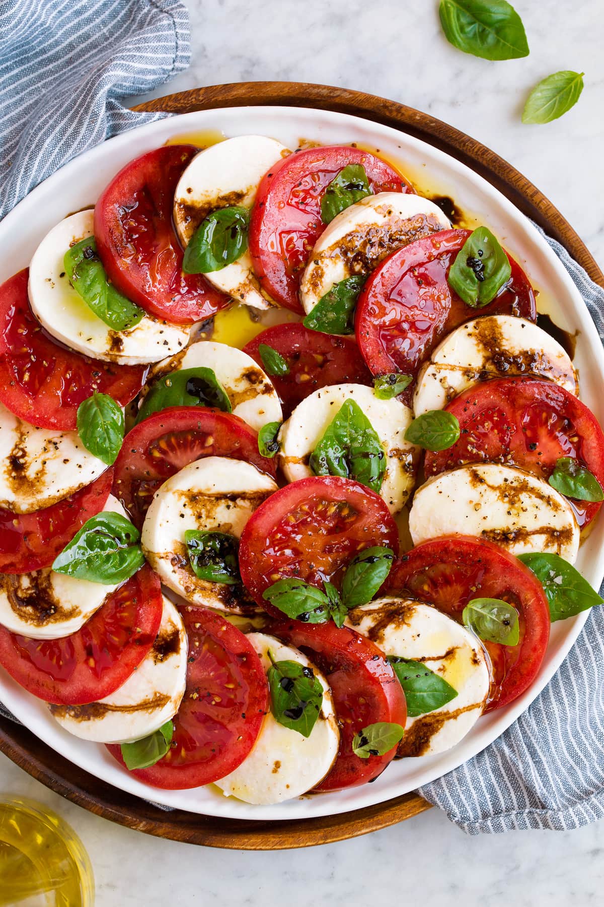 Caprese salad layered in a pretty design shown on a white platter. Overhead image of carpese salad with balsamic glaze on a white platter.