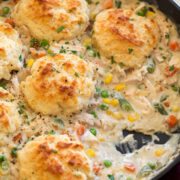 Image of Chicken Pot Pie with Biscuits shown in a cast iron skillet with a scoop removed from pot pie.