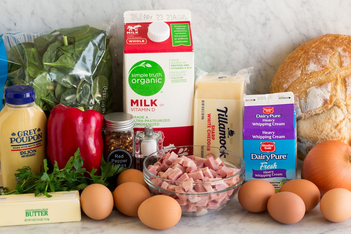 Strata Photo of ingredients used to make a strata. Includes bread, eggs, onion, cream, cheddar cheese, milk, ham, red pepper flakes, bell pepper, spinach, dijon mustard and butter.