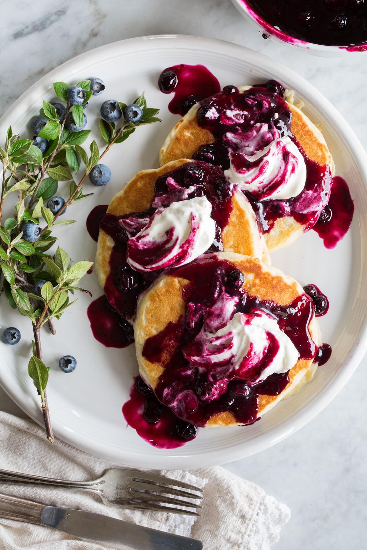 Blueberry Syrup Blueberry syrup shown poured over pancakes with whipped cream on top.