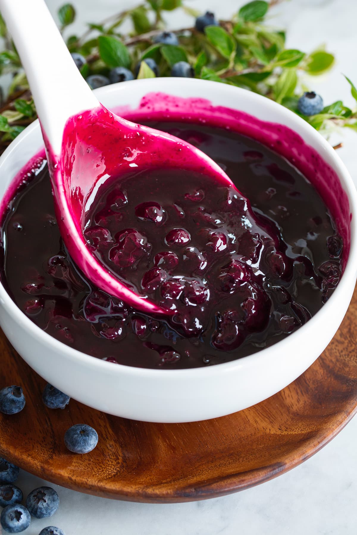 Blueberry Syrup Finished blueberry syrup in a white bowl over a wooden plate. Syrup is being scooped by a large white ladle.