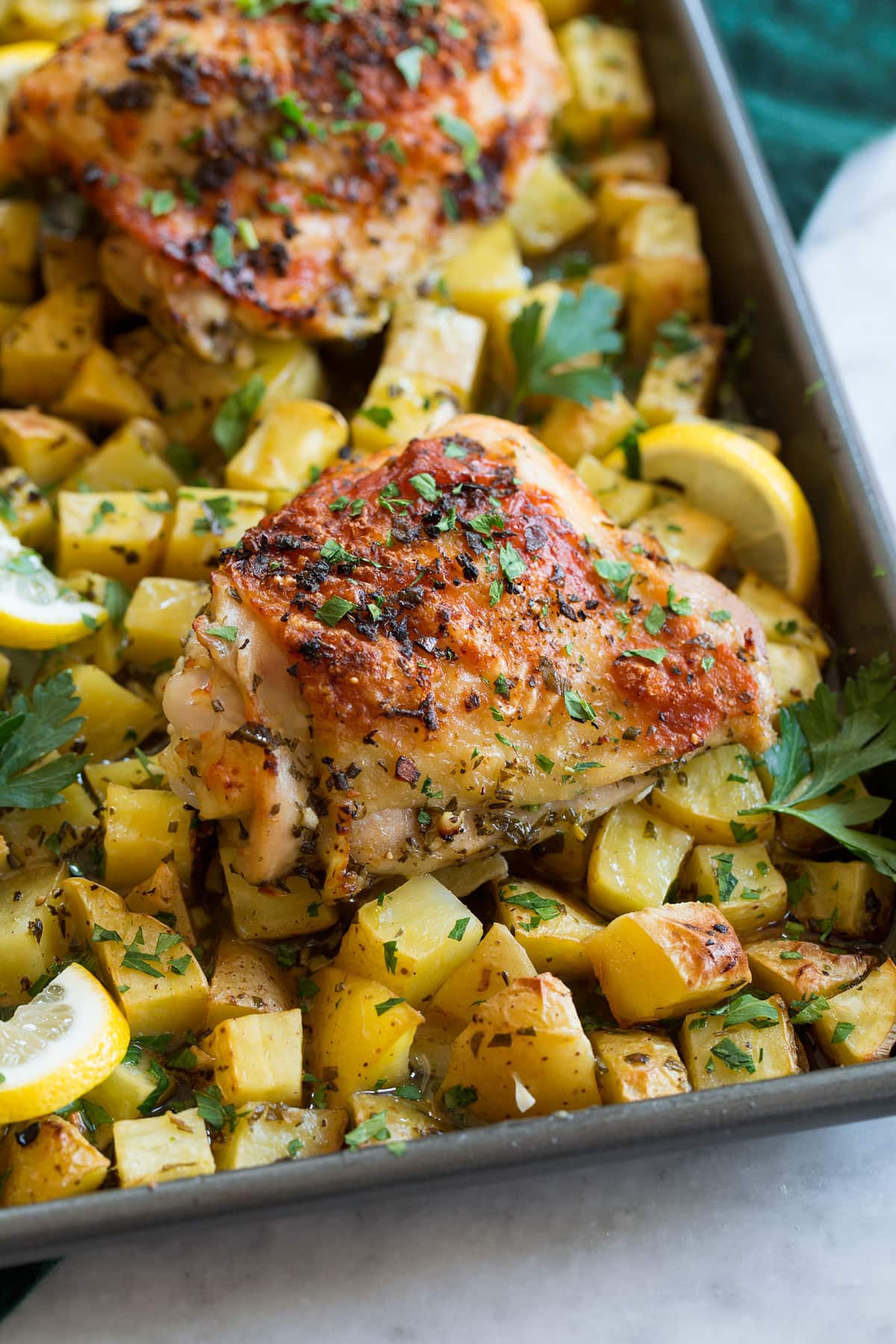Baked Lemon Chicken and Potatoes Close up photo of lemon chicken thighs and potatoes on a baking sheet.