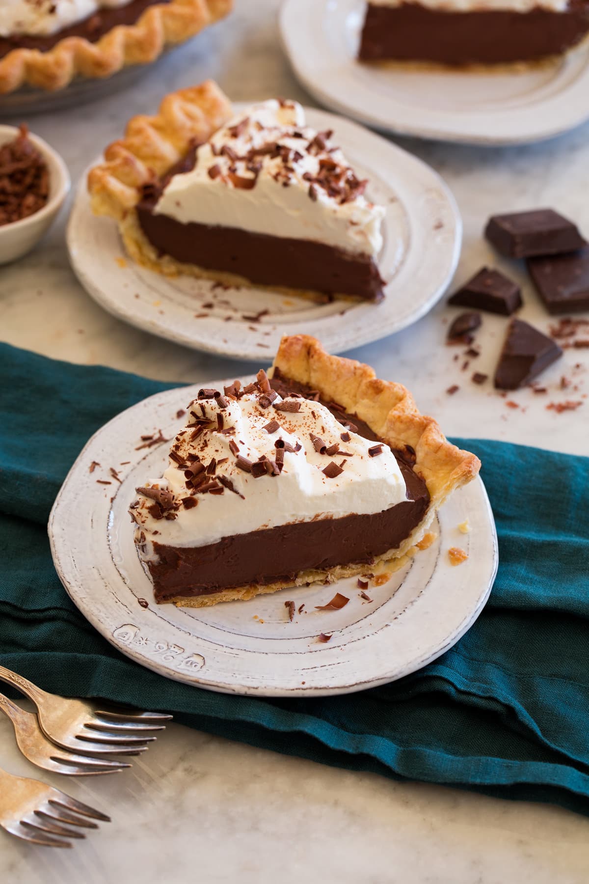 Chocolate Cream Pie Two slices of chocolate cream pie on small white dessert plates set over a blue cloth on a marble surface with chocolate chunks and curls in the backround.