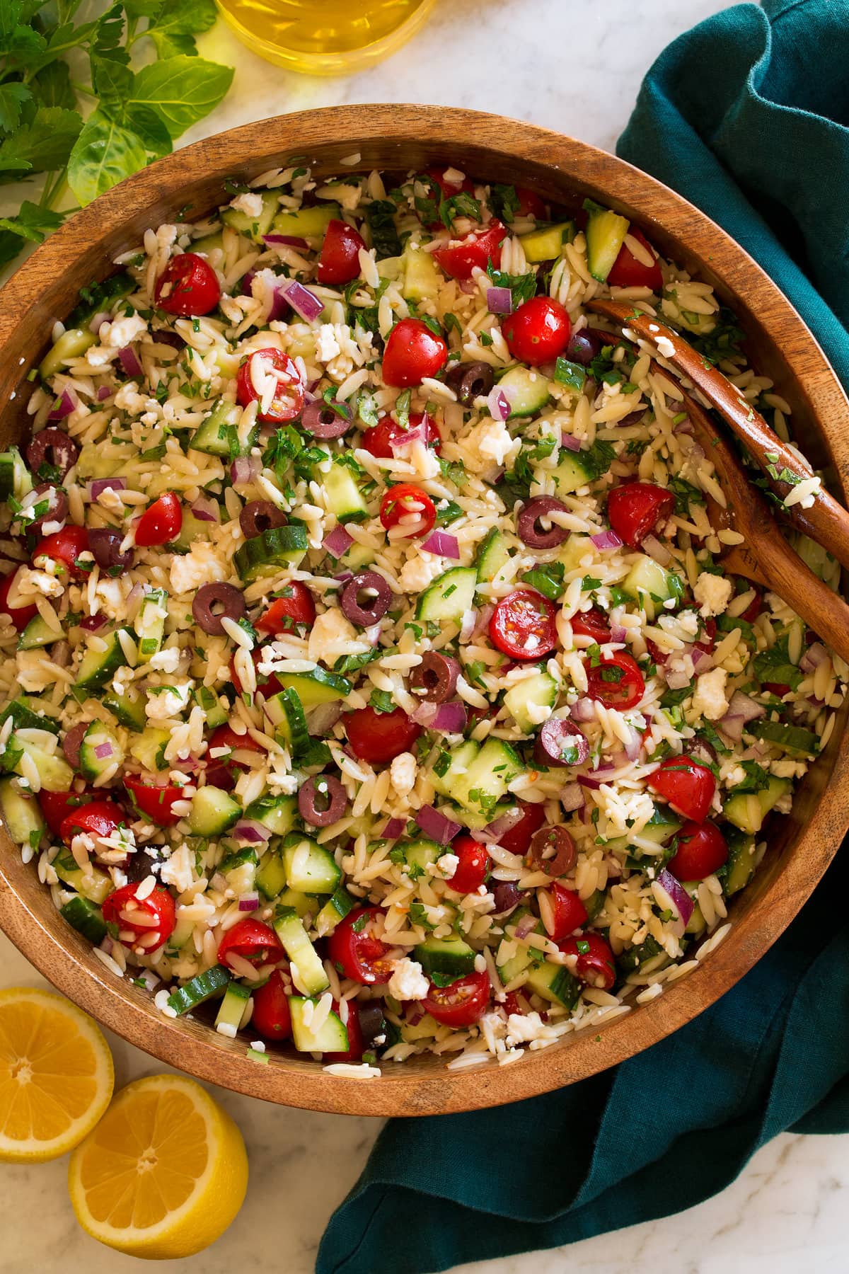 Orzo pasta salad in a large wooden bowl on a marble surface.