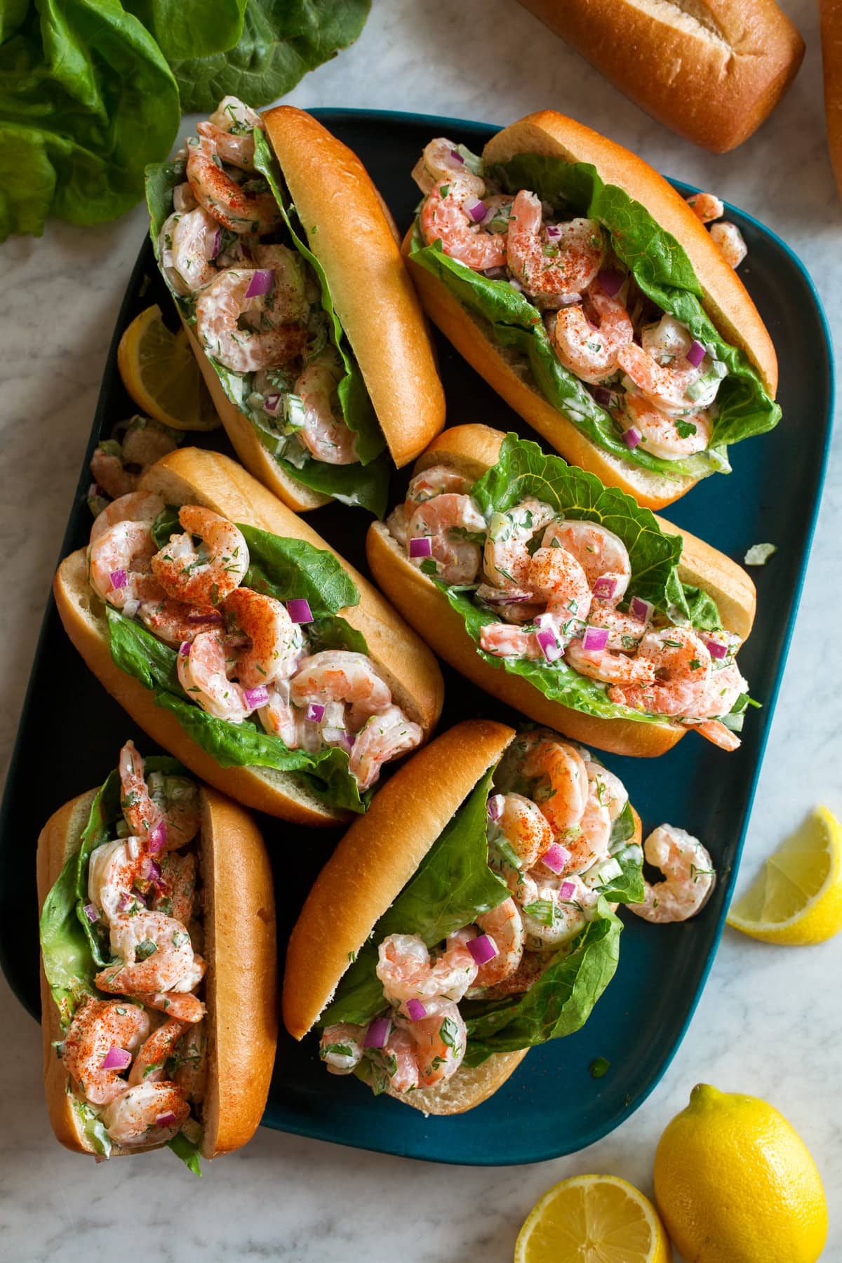 Shrimp Salad Shrimp Salad shown served in hoagie buns with lettuce leaves on a blue rectangular platter from above.
