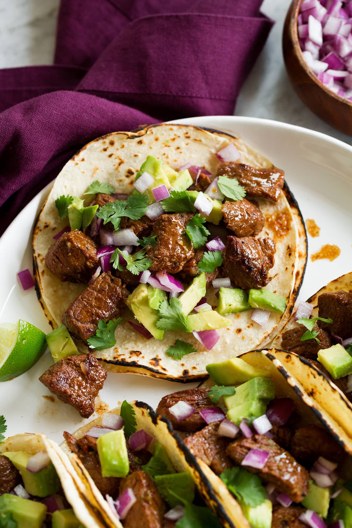 Steak Tacos Single steak taco with avocado, cilantro and red onion shown close up.