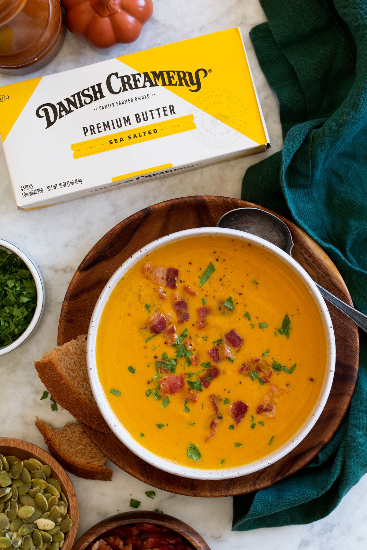 Pumpkin Soup Pumpkin soup in a white bowl over a wooden plate with wheat bread and butter to the side.