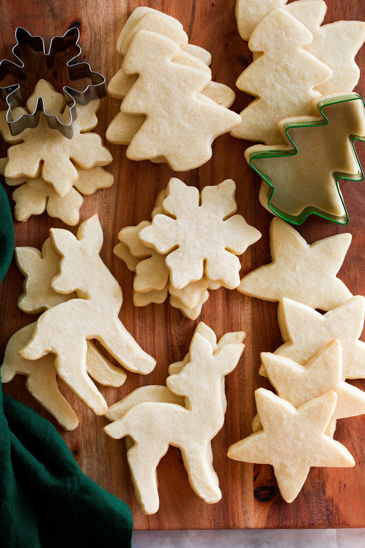 Sugar Cookie Cutout Recipe Baked cutout sugar cookies without icing shown on a wooden board with cookie cutters.