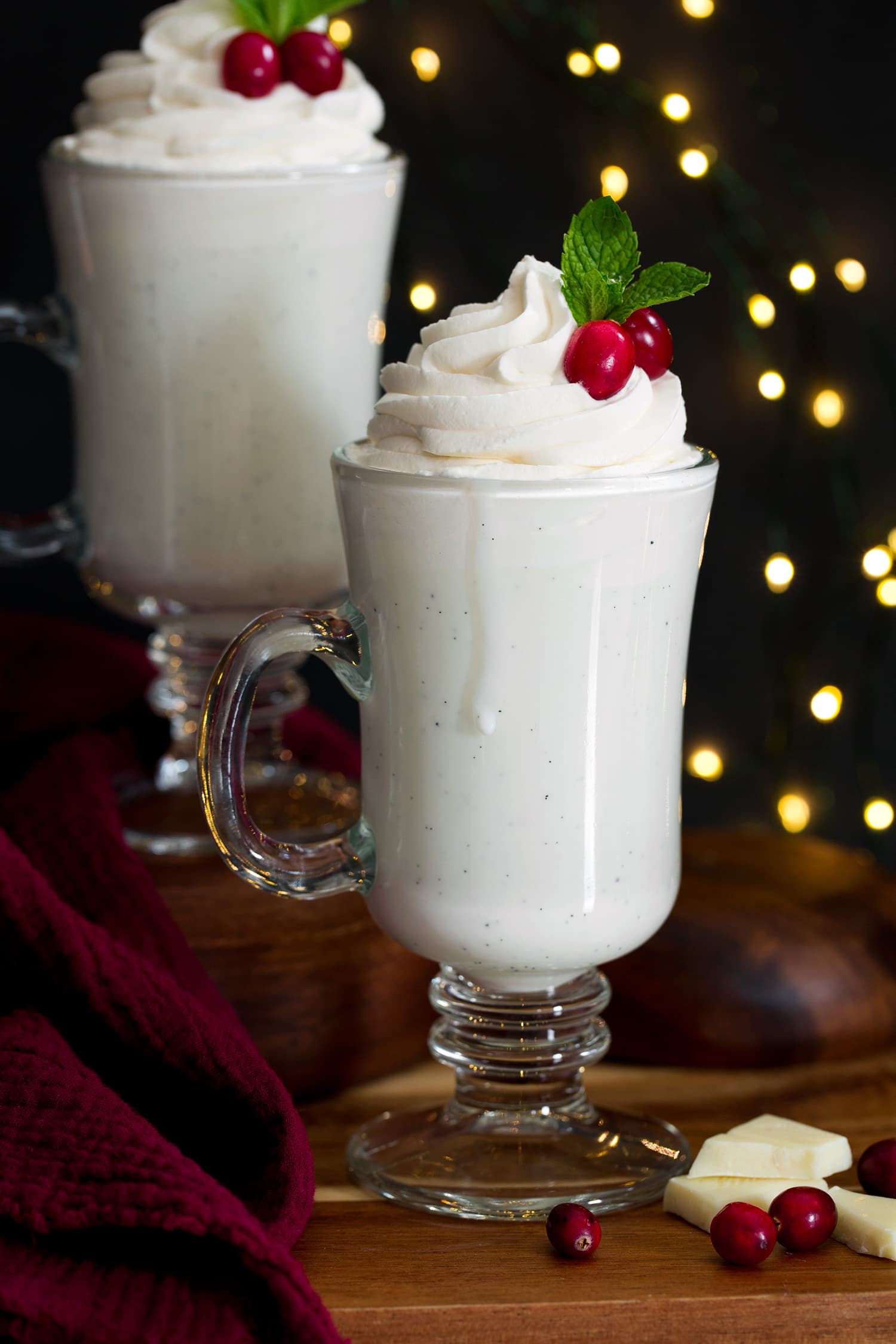 White Hot Chocolate Close up photo of tall glass of white hot chocolate topped with whipped cream, cranberries and mint.