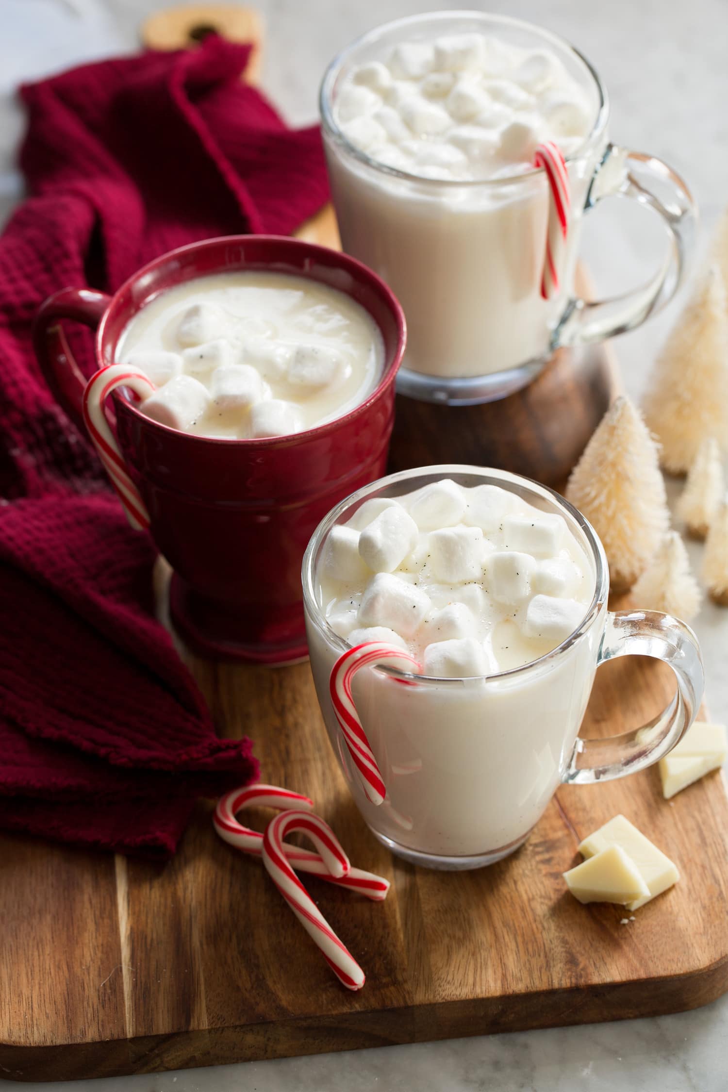 White Hot Chocolate Three cups of white hot chocolate topped with marshmallows and a peppermint candy cane hanging on each mug.