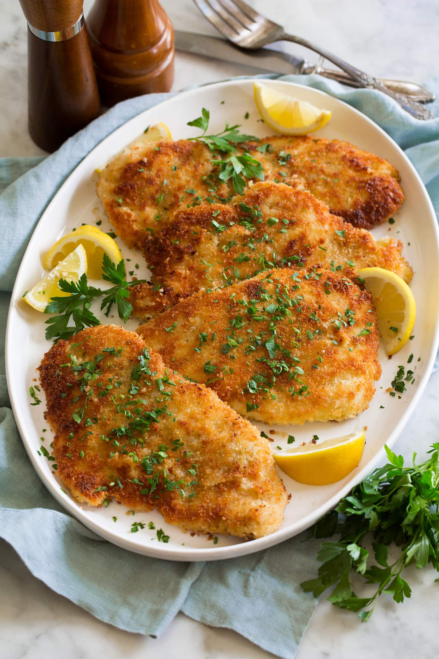 Tray with four servings of flattened and breaded golden brown chicken schnitzel.