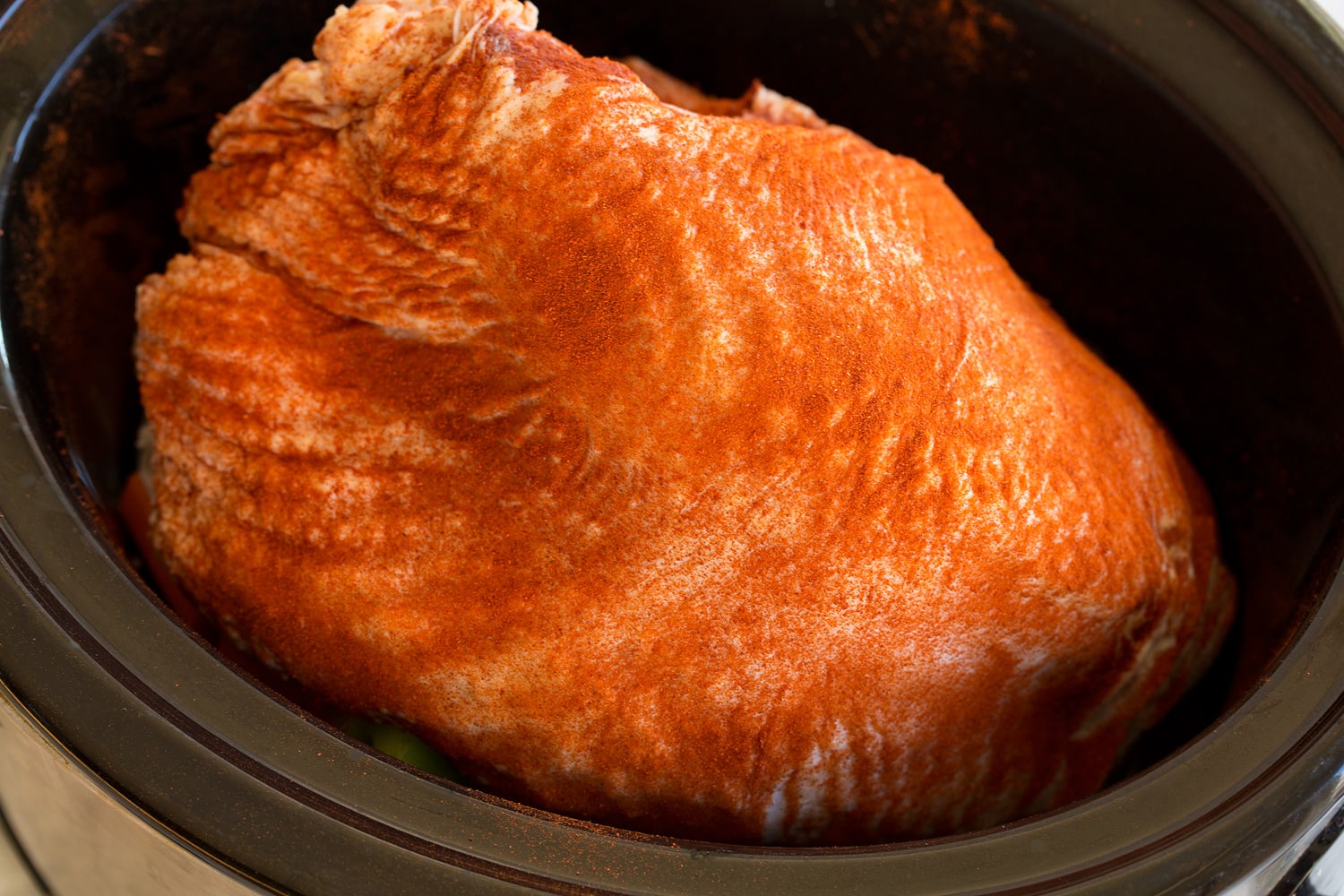 Crockpot Turkey Breast Raw turkey breast being added to slow cooker over veggies.