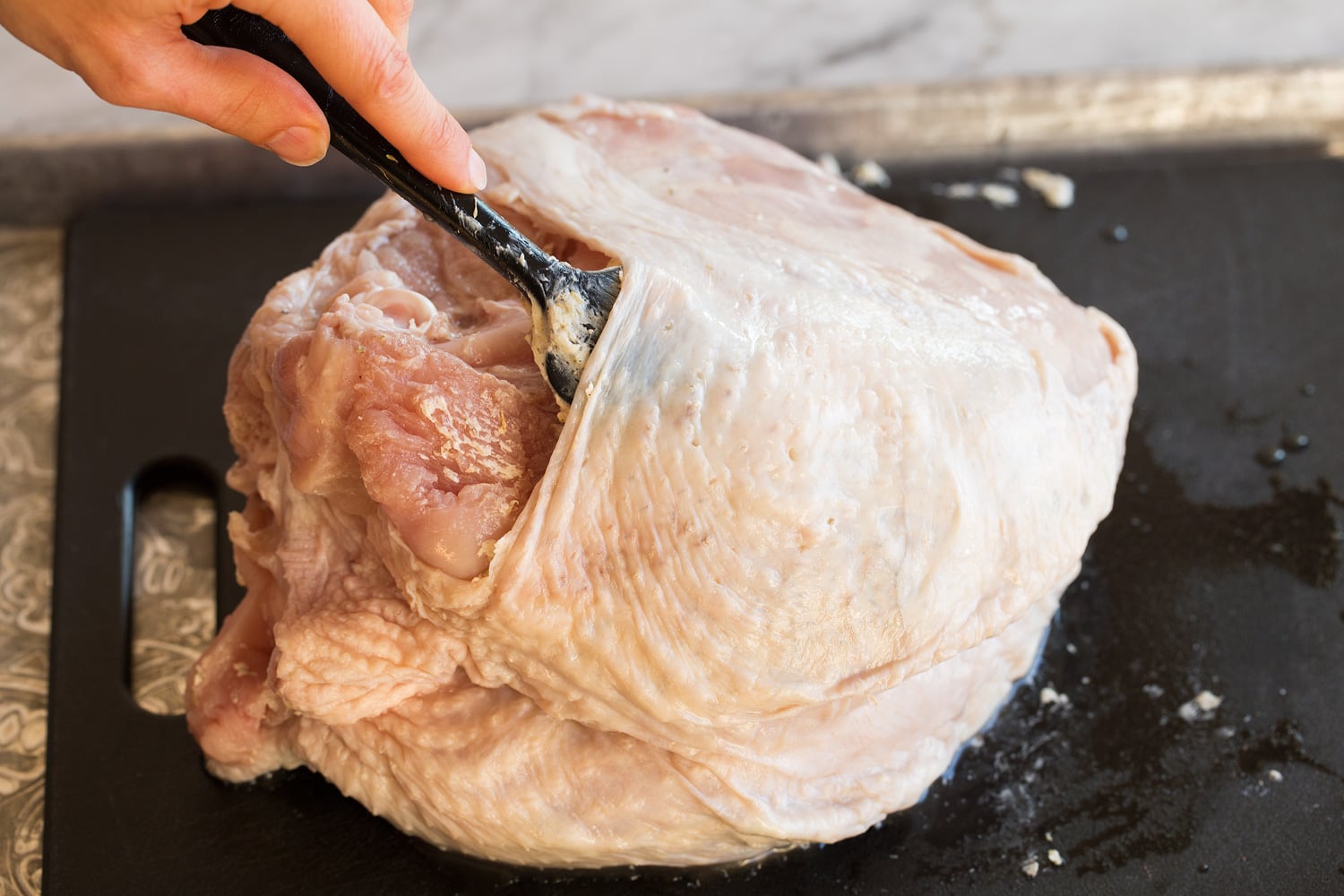 Slow Cooker Turkey Breast Adding butter herb mixture to a raw turkey breast under skin.