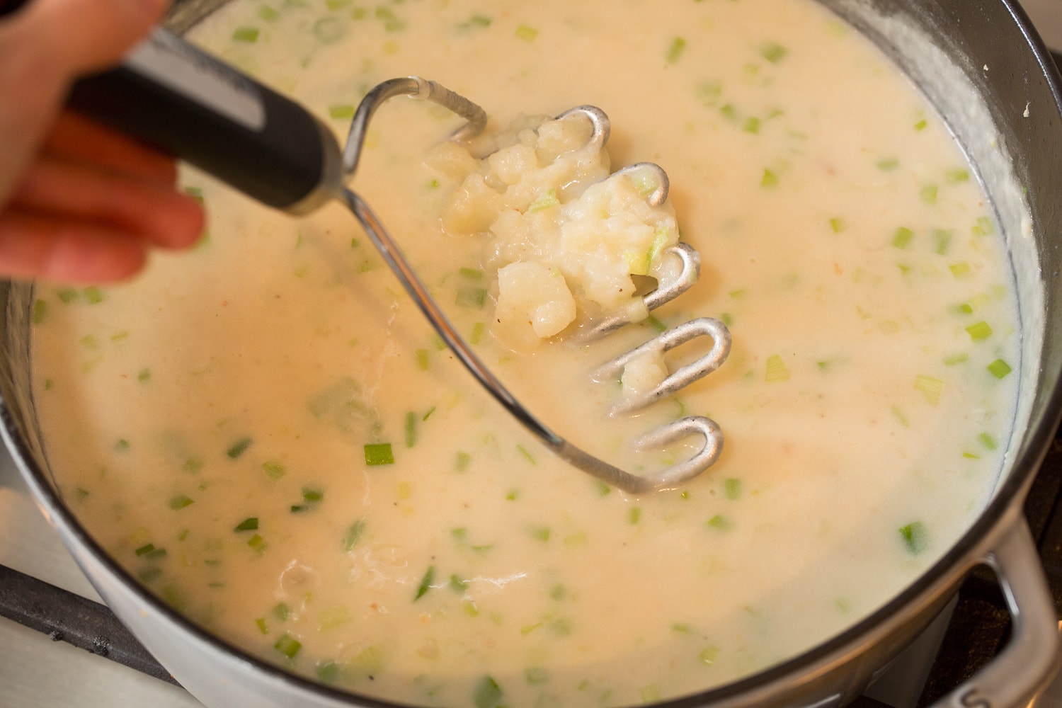 Baked Potato Soup Mashing potatoes in pot of soup.