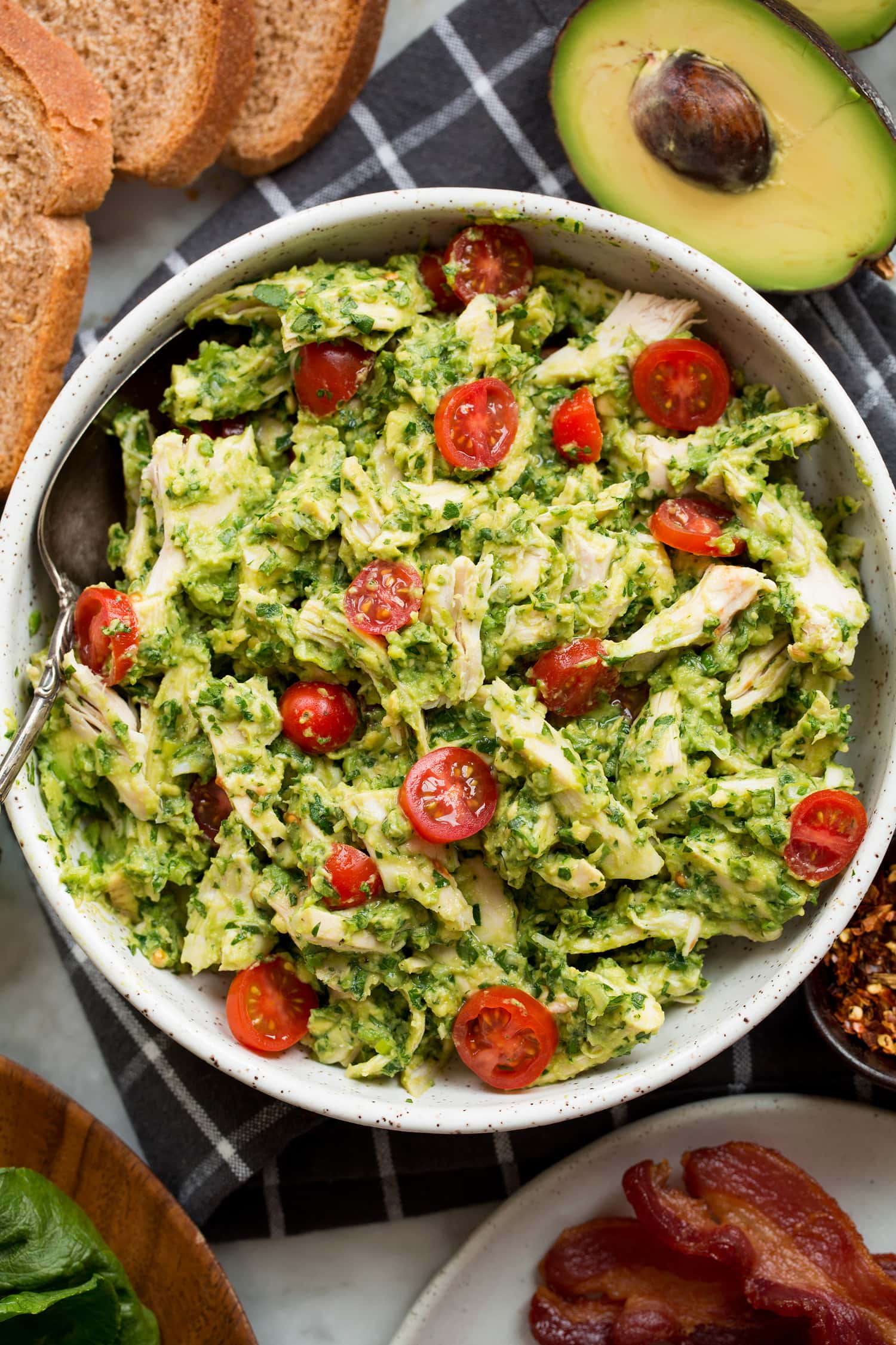 Avocado Chicken Salad Avocado chicken salad with shredded chicken, mashed, avocado, tomato and bacon on the side.
