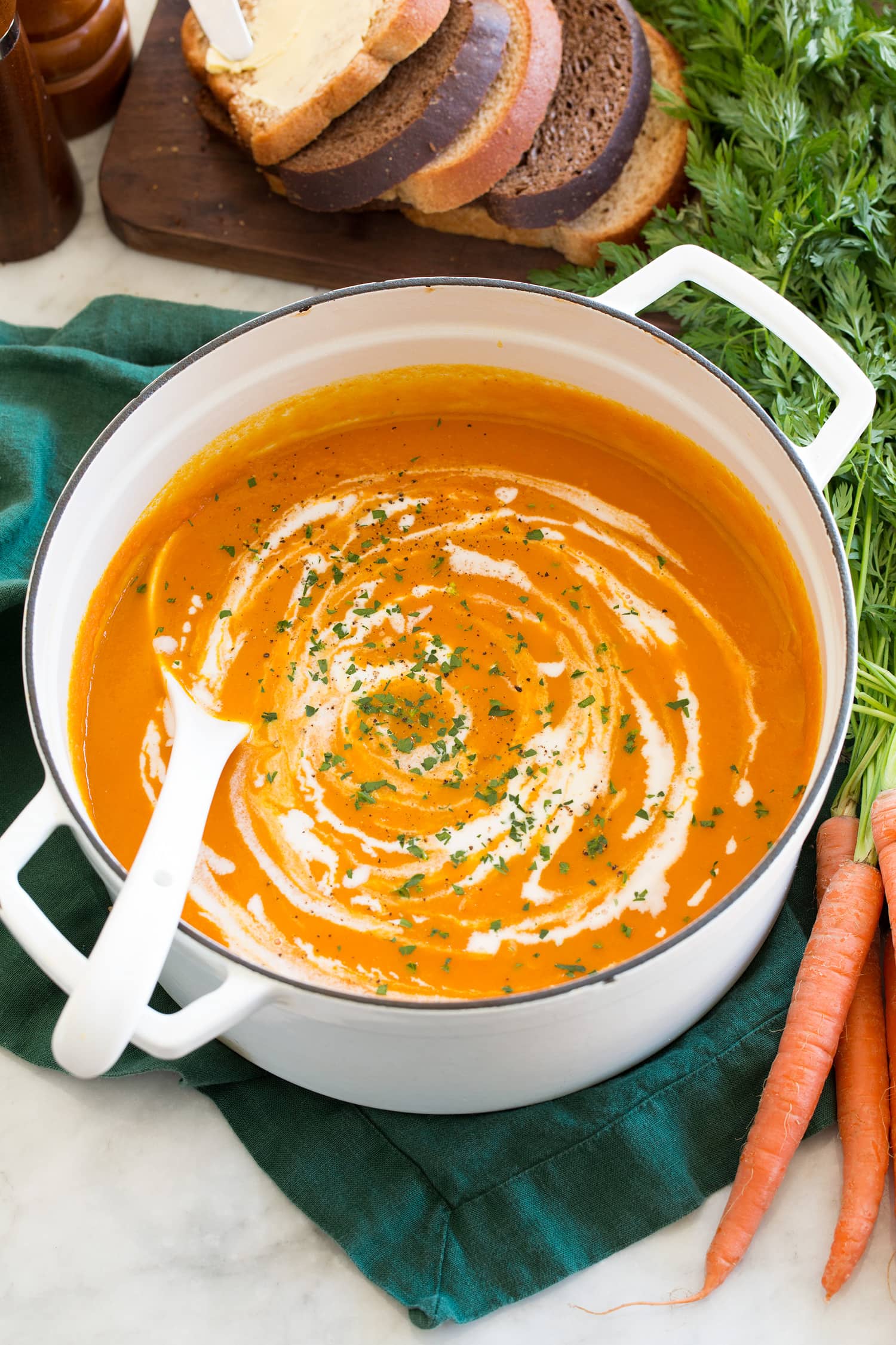 Carrot Soup Carrot soup shown in a white enameled pot over a green cloth with fresh carrots to the side.