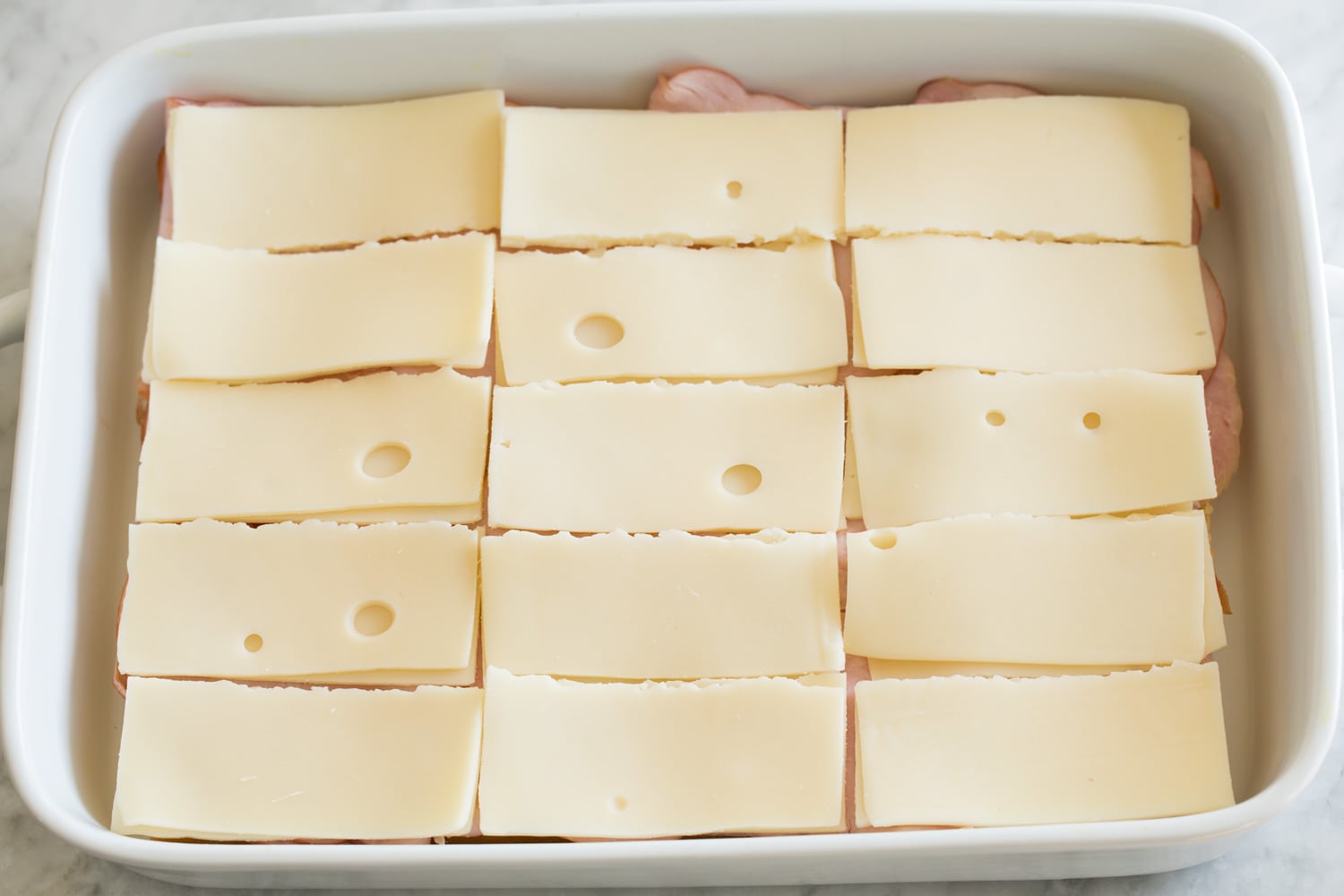 Ham and Cheese Sliders Layering swiss cheese over ham layer of sliders.