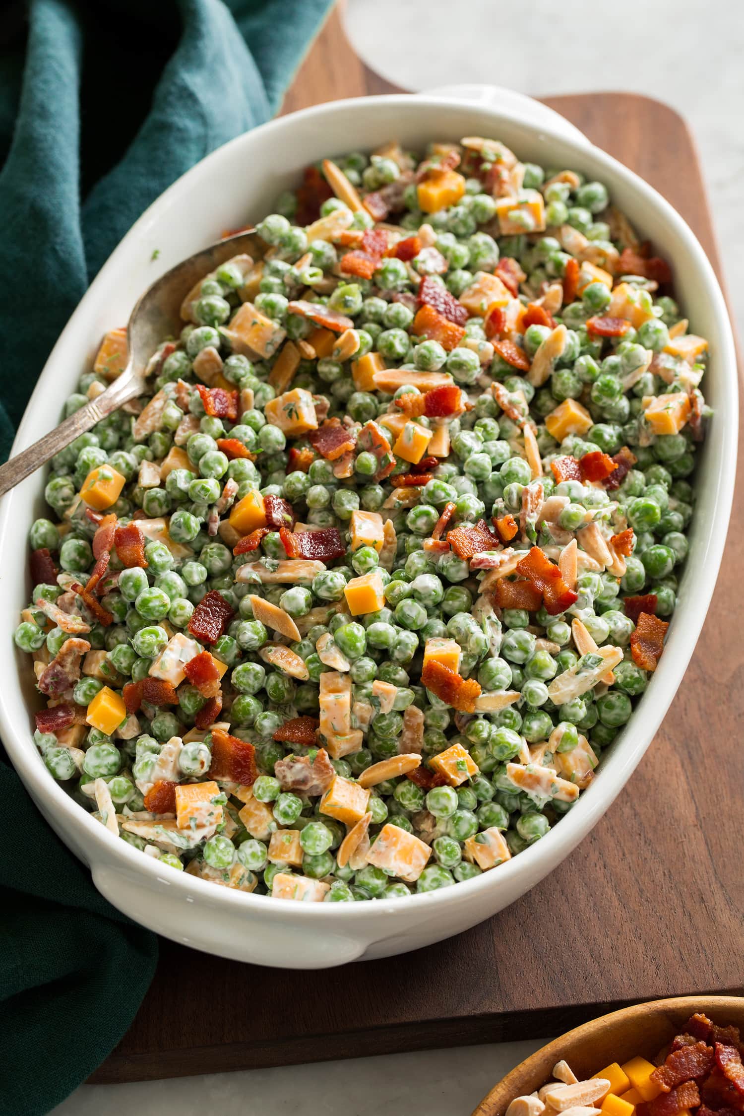 Pea Salad Pea salad with cheddar and bacon shown in an oval serving dish over a wooden board.