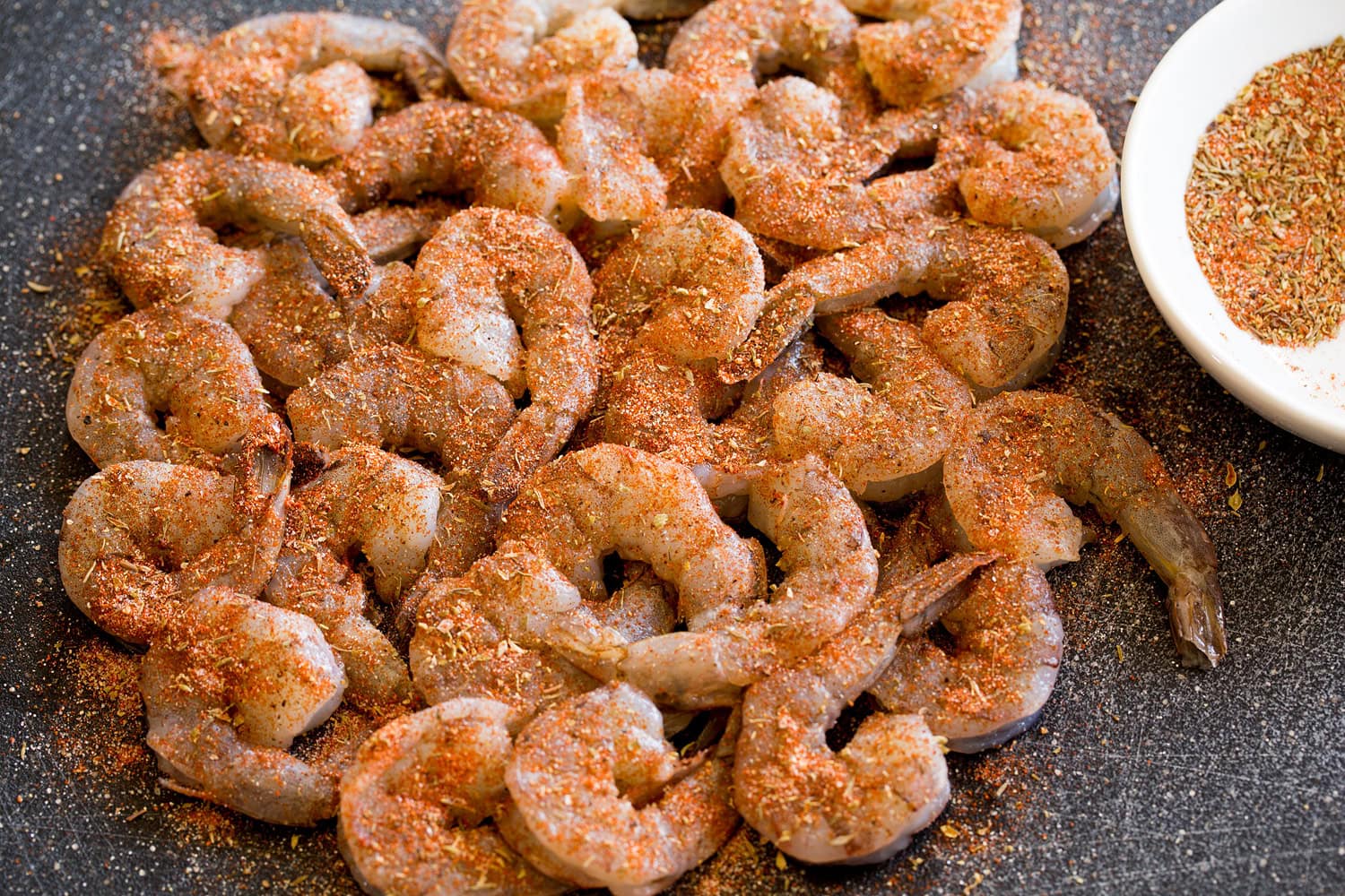 Blackened Shrimp Raw shrimp sprinkled with blackening seasoning on a black cutting board.