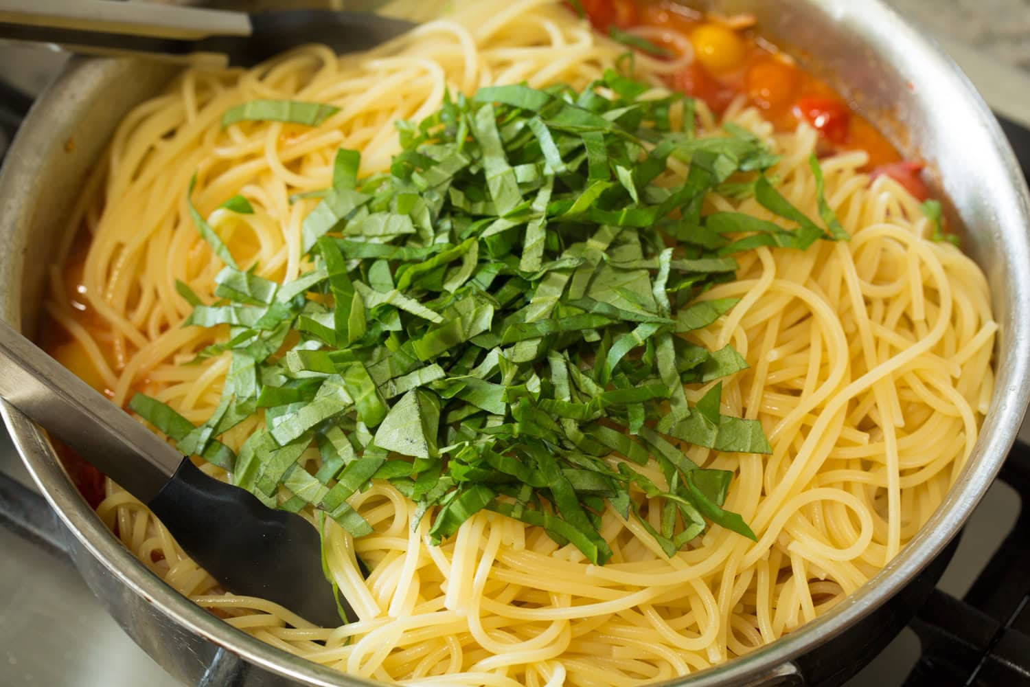 Cherry Tomato Pasta Basil and pasta being added to sauce.